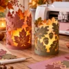 Herfstlichtjes maken met papieren lantaarnhoezen en je plotter Twee papieren herfstlantaarns met bladmotieven en veilige LED-lampjes op een warme knutseltafel